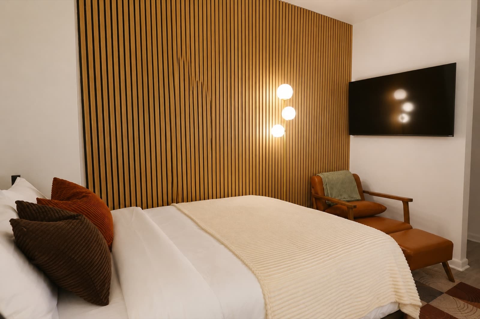 Furnished studio with ensuite bathroom at Amsterdam Place, Upper West Side NYC — bed against the oak slat accent wall with reading sconces