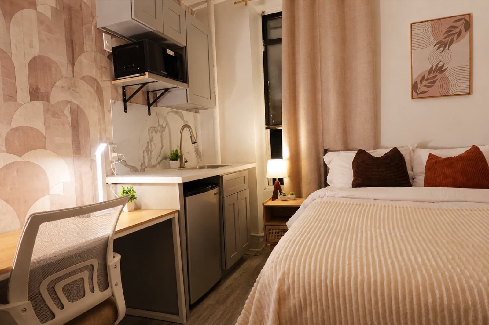 Furnished studio with private shower at Amsterdam Place, Upper West Side NYC — desk and kitchenette beside the arched-print wallpaper