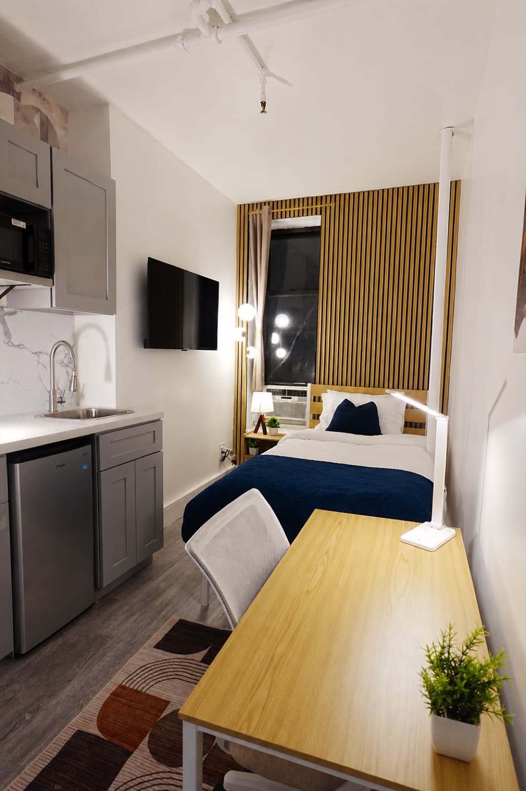 Deluxe furnished room at Amsterdam Place, Upper West Side NYC — kitchenette and bed, vertical view