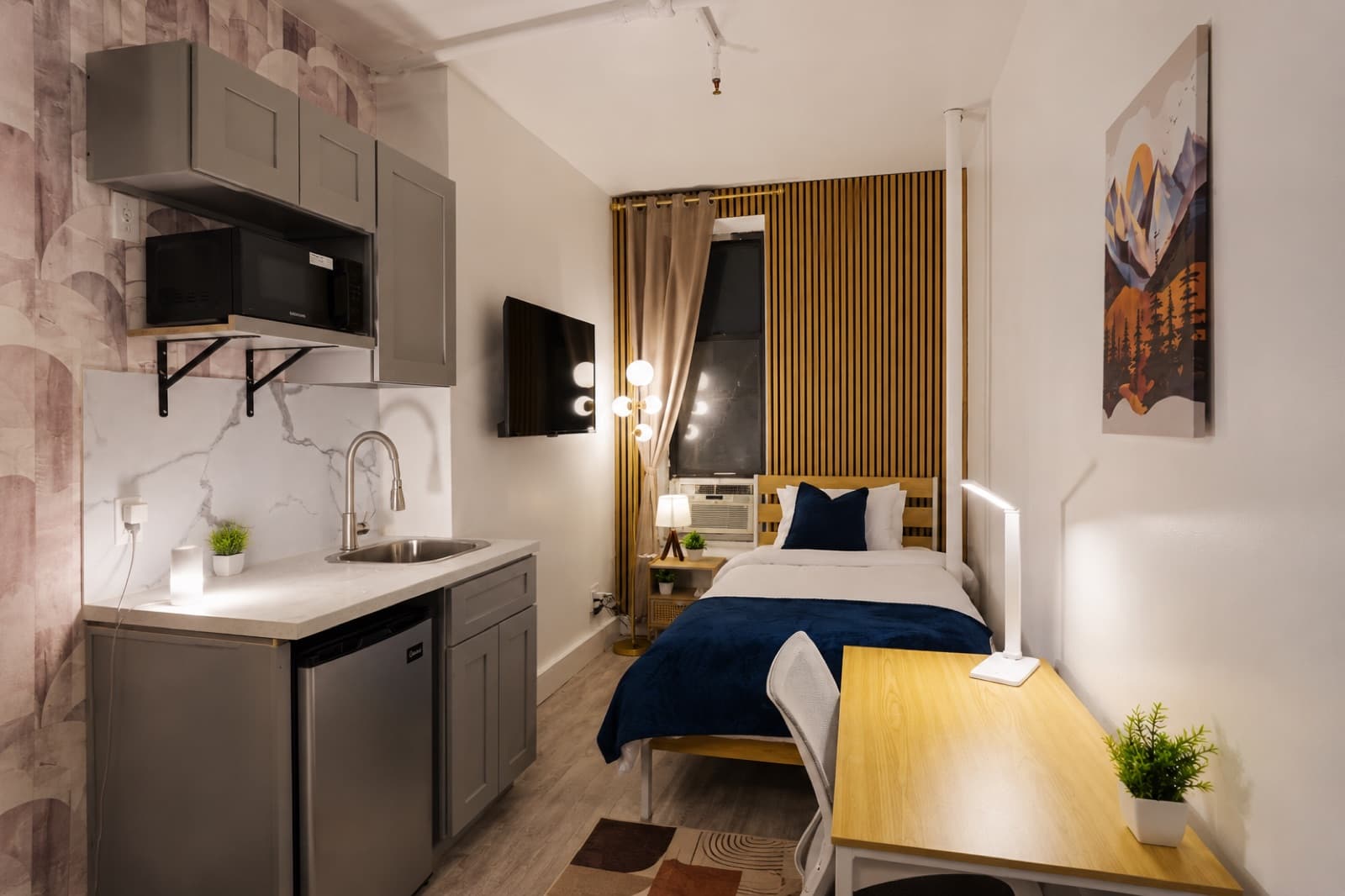 Deluxe furnished room at Amsterdam Place, Upper West Side NYC — kitchenette and bed with a marble backsplash