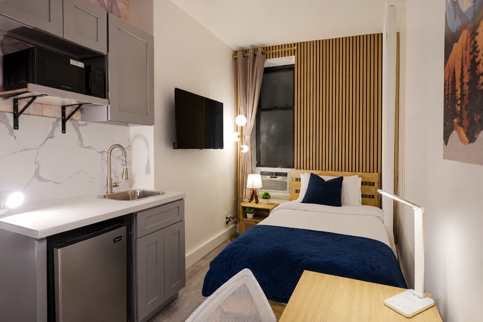 Deluxe furnished room at Amsterdam Place, Upper West Side NYC — kitchenette and bed beneath the oak slat wall